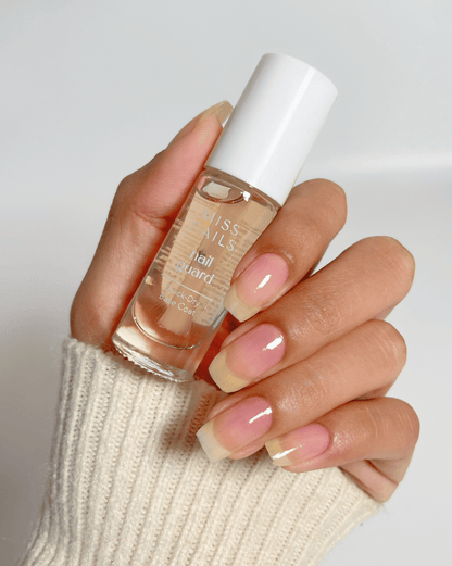 Hand holding a bottle of quick dry base coat from manicure kit, with matching nails against a neutral background