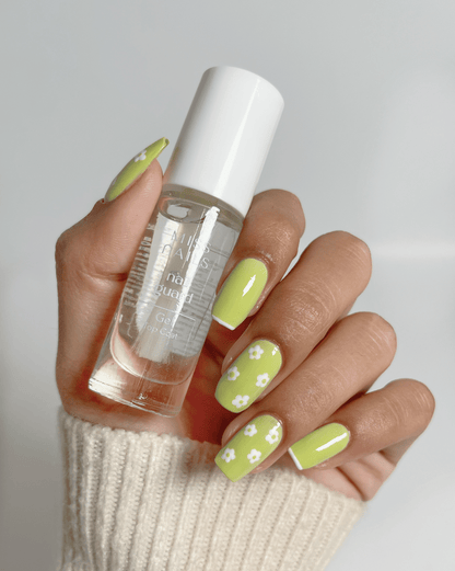 Hand holding a bottle of gel top coat with light green nails and white floral designs.