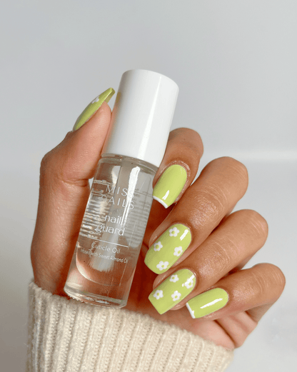 Hand holding a bottle of nail care  nail oil product with light green nail polish on a neutral background